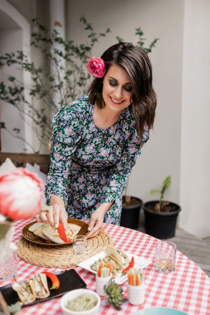 Woman serving Mexican food at outdoor garden party with floral decor.